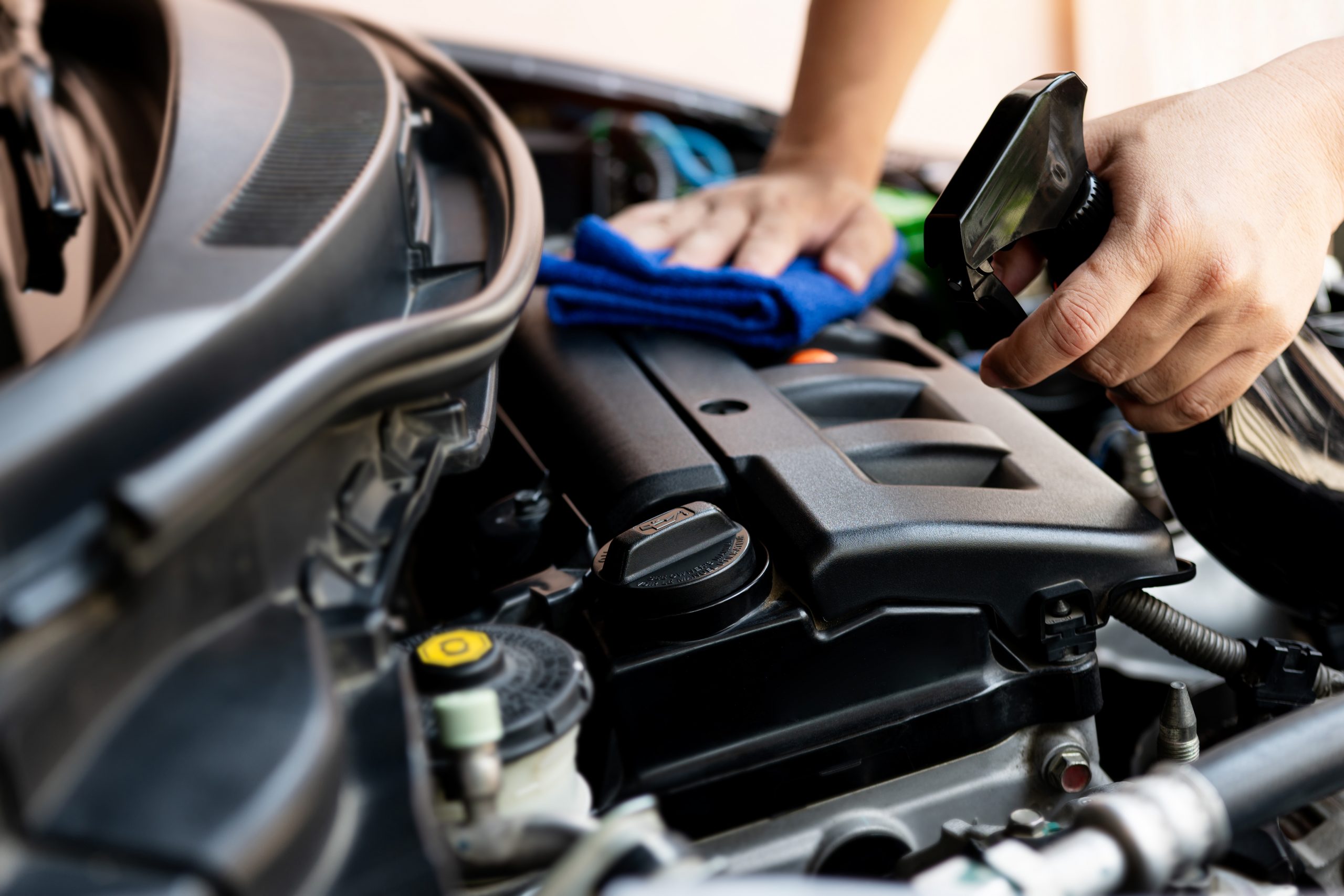 man's hand holding a blue microfiber cloth and wiping the top of an engine block down with a spray bottle in the other hand